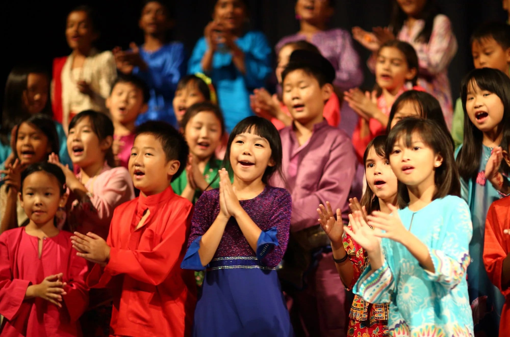 Children in cultural costumes from several countries singing together on a school stage