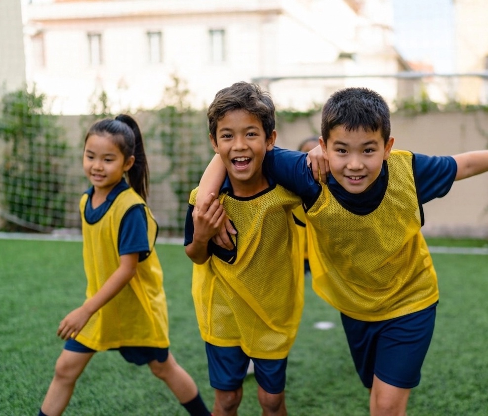 Three young children in yellow training bibs on the football pitch at ISJ