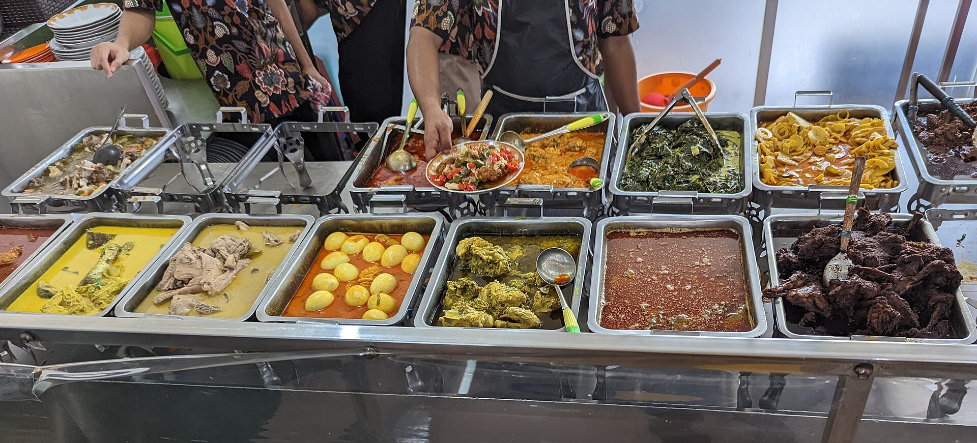 Display of Indonesian dishes at a Jakarta Padang restaurant, with curries, vegetables, and fish spread across a counter