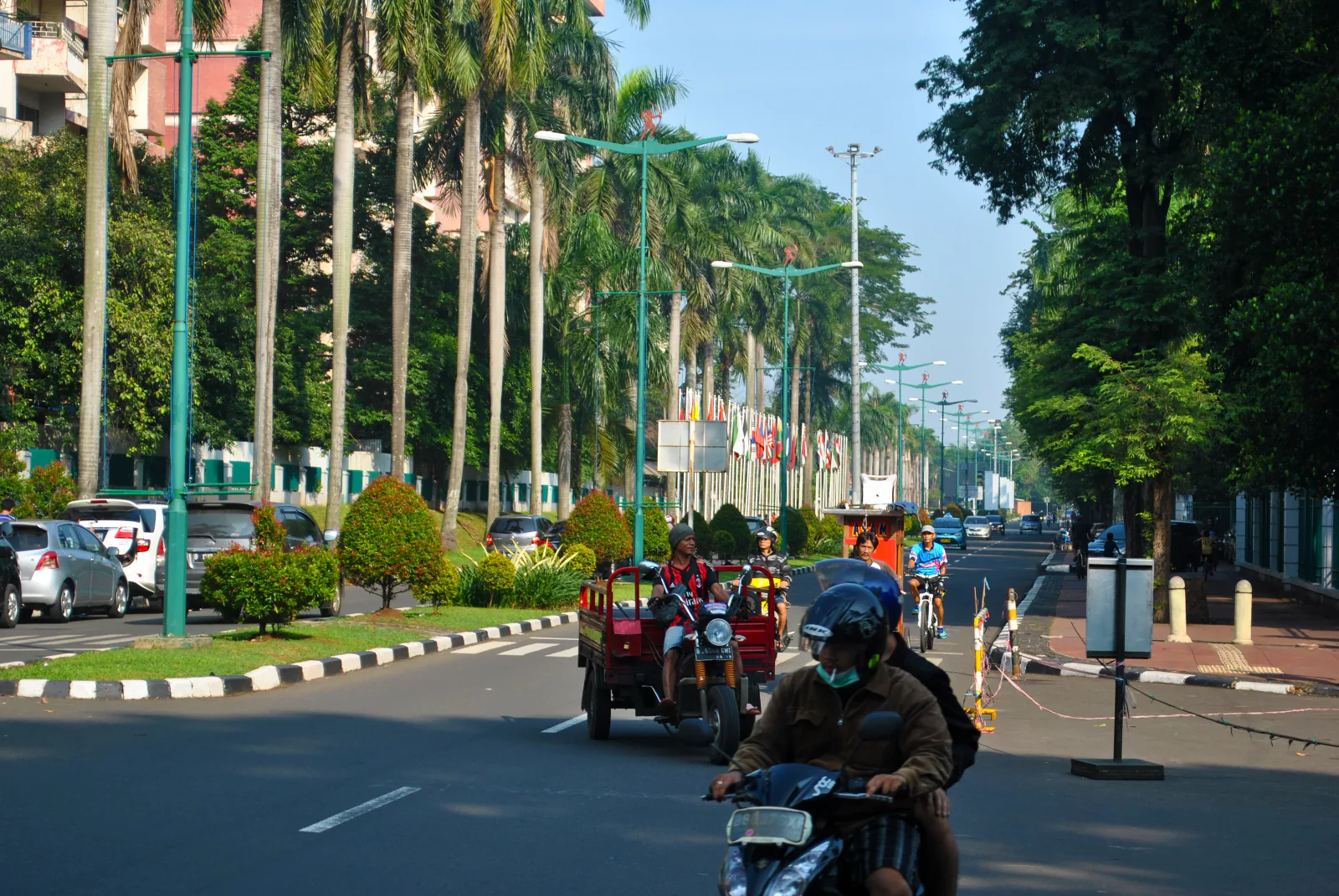 Wide tree-lined boulevard in the Gelora Bung Karno complex, Central Jakarta, with cyclists and motorbikes