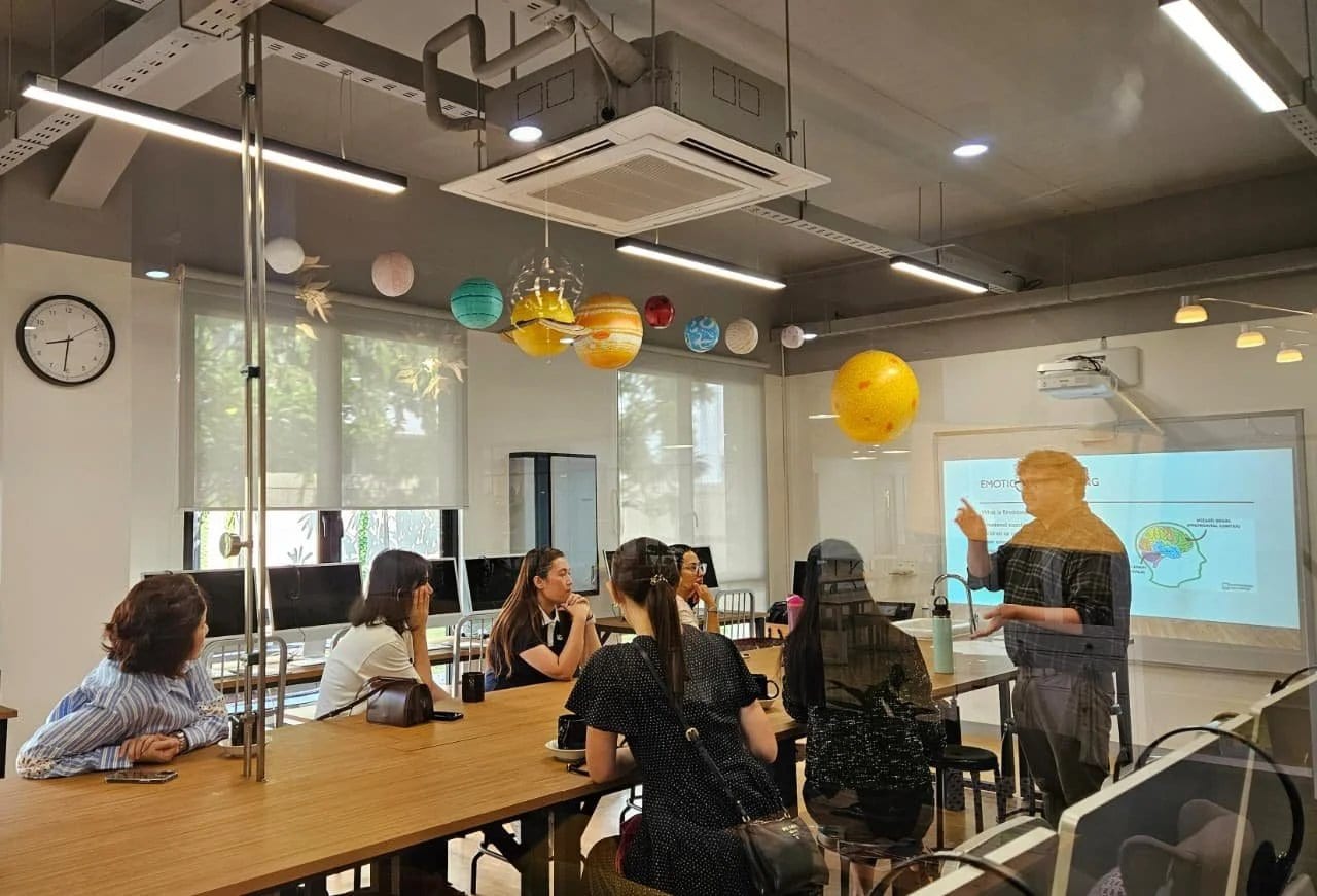 Parents seated around a long table in a school room, watching a presentation on emotions with a brain diagram on screen
