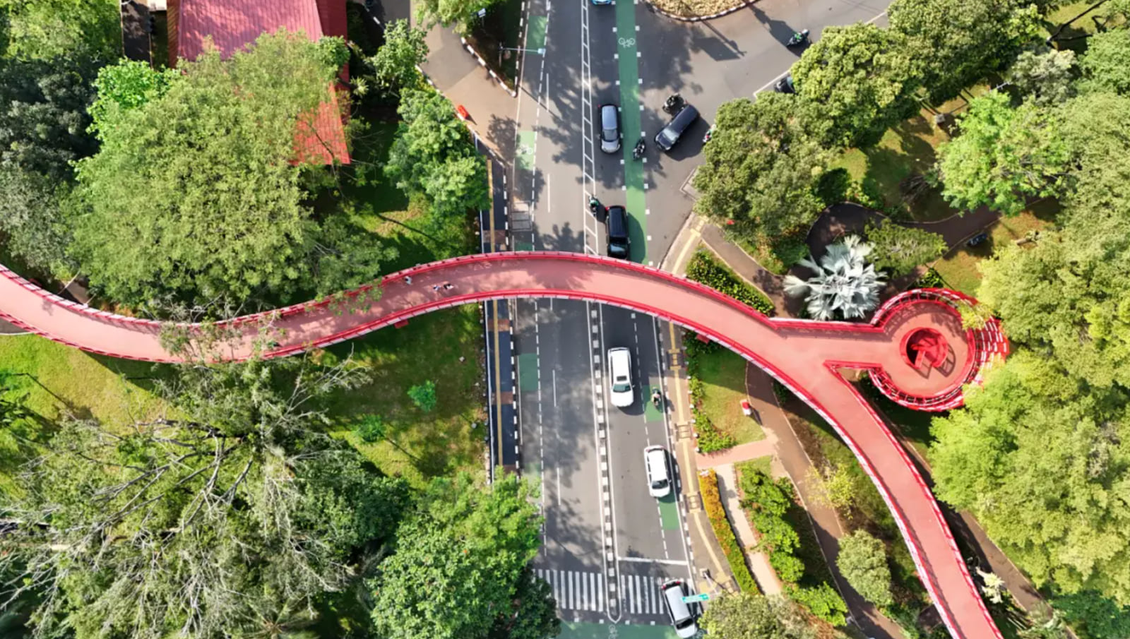 The red skybridge curving through the treetops at Taman Bendera Pusaka, seen from above