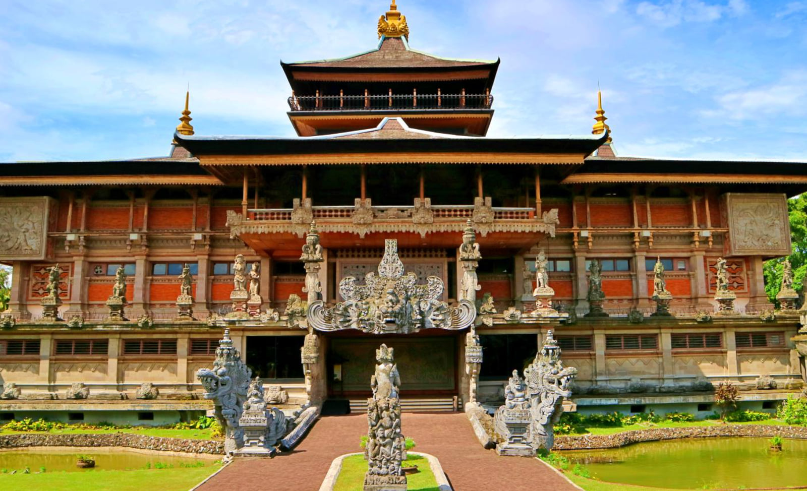A carved pavilion with a tiered roof and stone gateway at Taman Mini Indonesia Indah