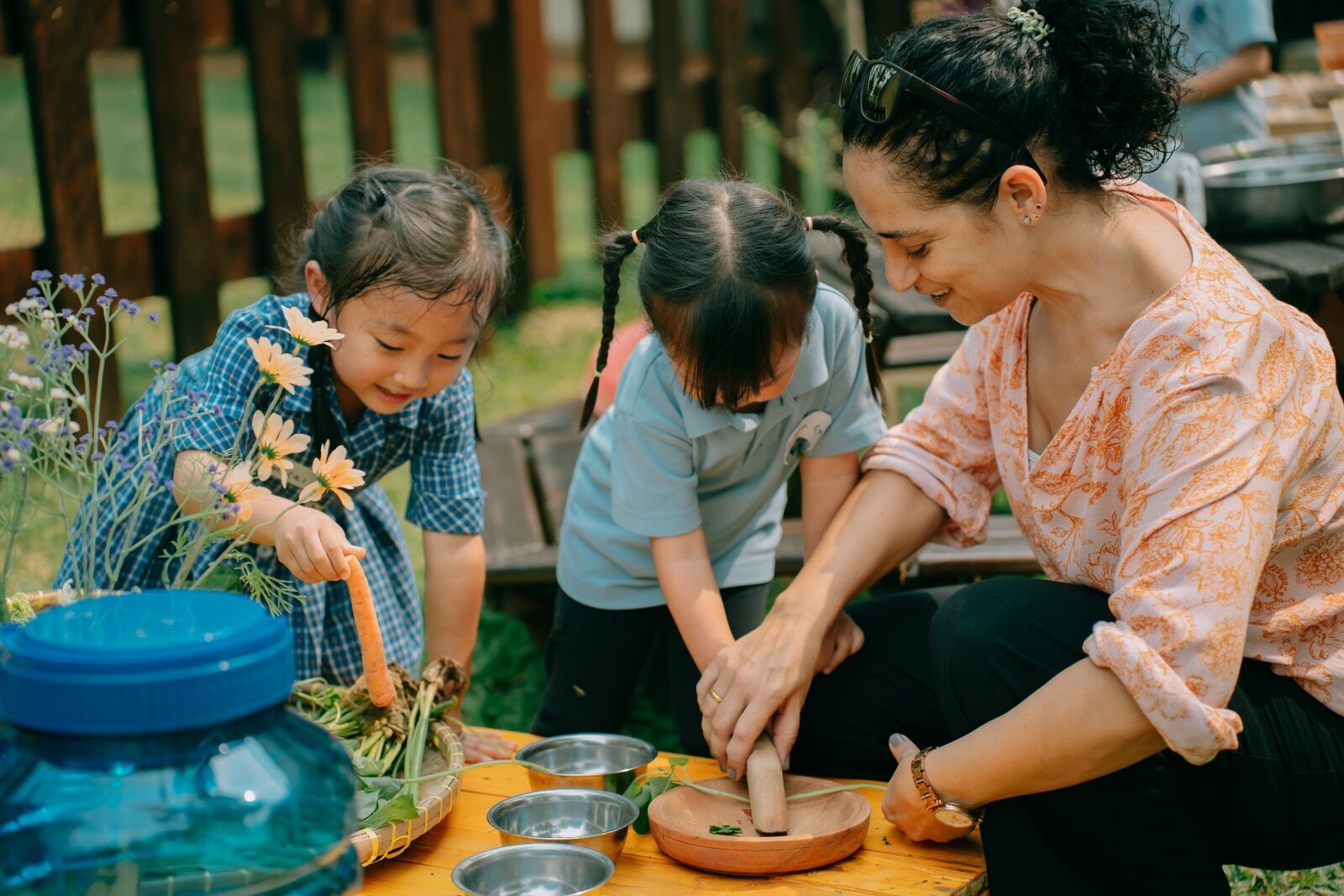 An ISJ teacher guiding two Early Years pupils through an outdoor cooking and herbs activity